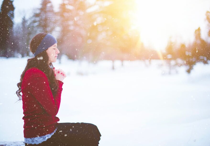 Une jeune femme assise dans la neige prie.