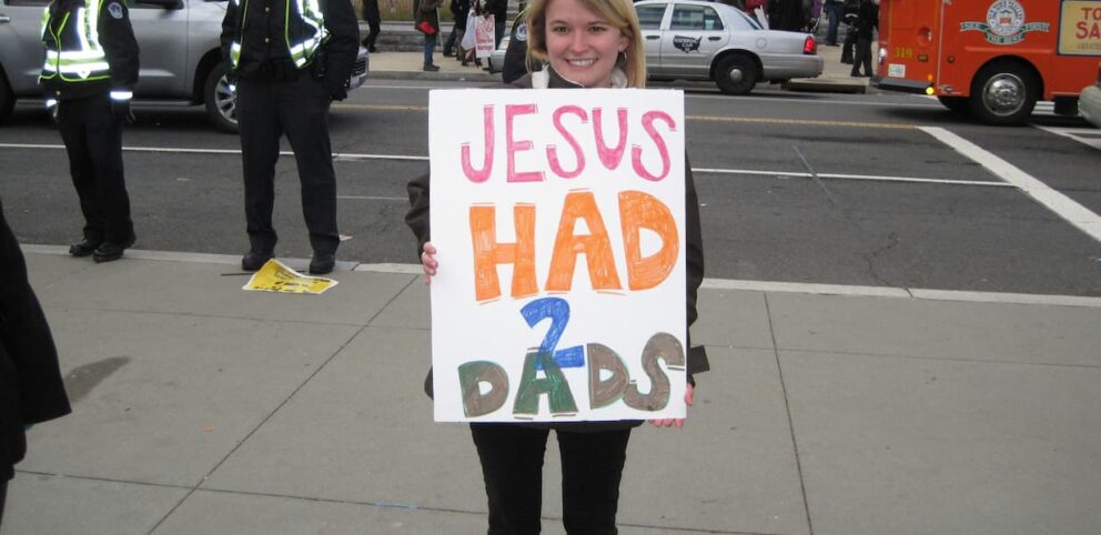 Une personne woke qui tient un poster affirmant que Jésus a deux papas.