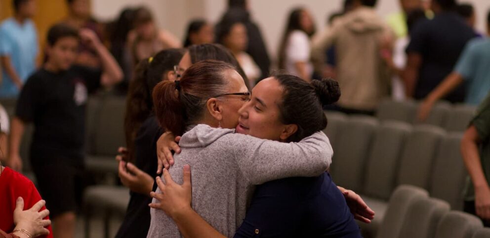 Deux femmes se donnent un câlin dans une église, symbole d'accueillir l'autre en Jésus.