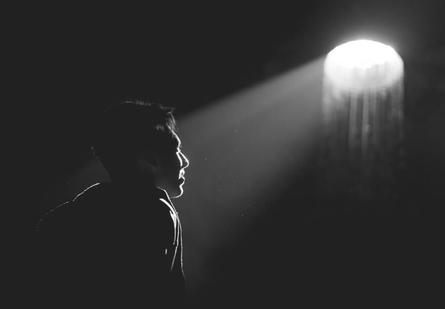 Un homme dans le noir regardant un lumière blanche se questionnant sur Dieu devant l'atrocité.