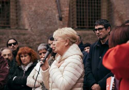 Femme âgée prenant parole au micro dans un rassemblement politique.