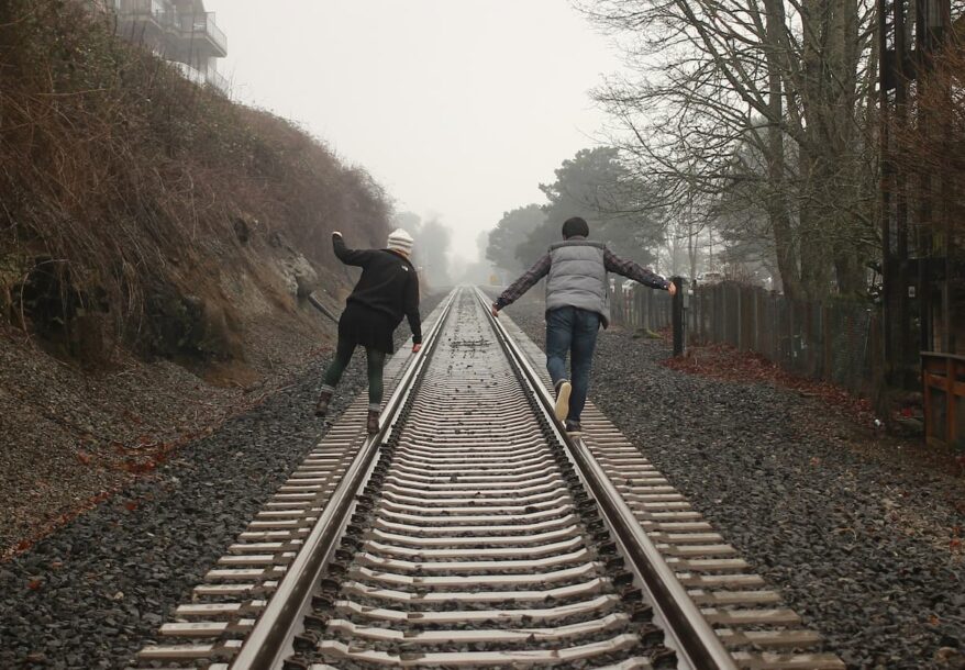 Deux personnes marchent en équilibre sur des rails, représentant le difficile équilibre de la loyauté envers son Église.