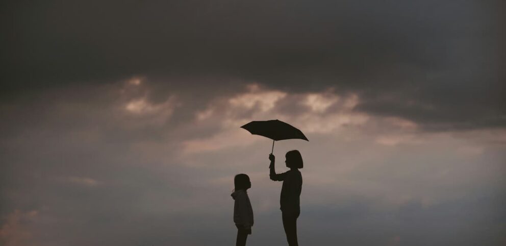 Une femme utilise un parapluie pour protéger un enfant, illustrant l'un des plus grands commandements.